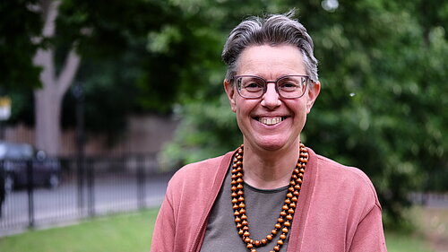 Photo of Janet Grauberg wearing a pink cardigan against a leafy green background